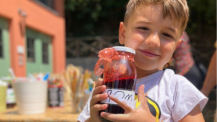 bambino sorridente tiene tra le mani un vasetto di marmellata