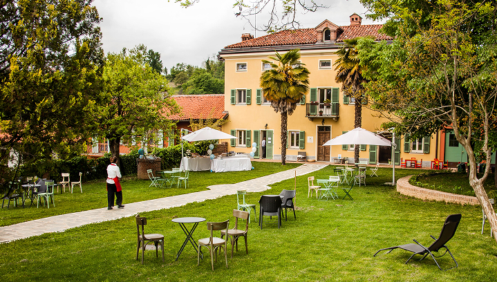 vista di un edificio con un ampio prato antistante, con alberi, tavoli e altri arredi da esterno