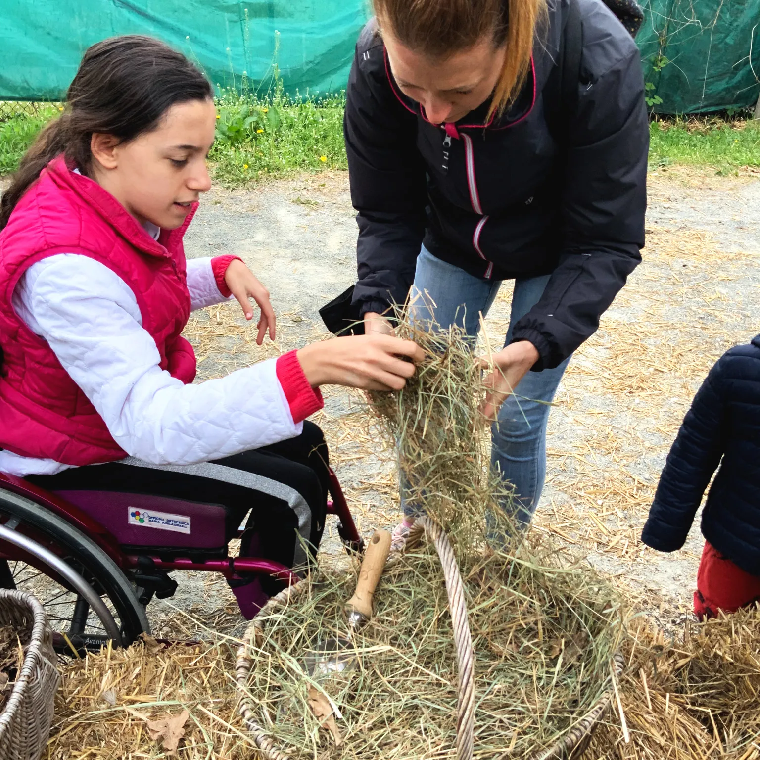 una donna prende del fieno da una cesta e lo porge a una bambina