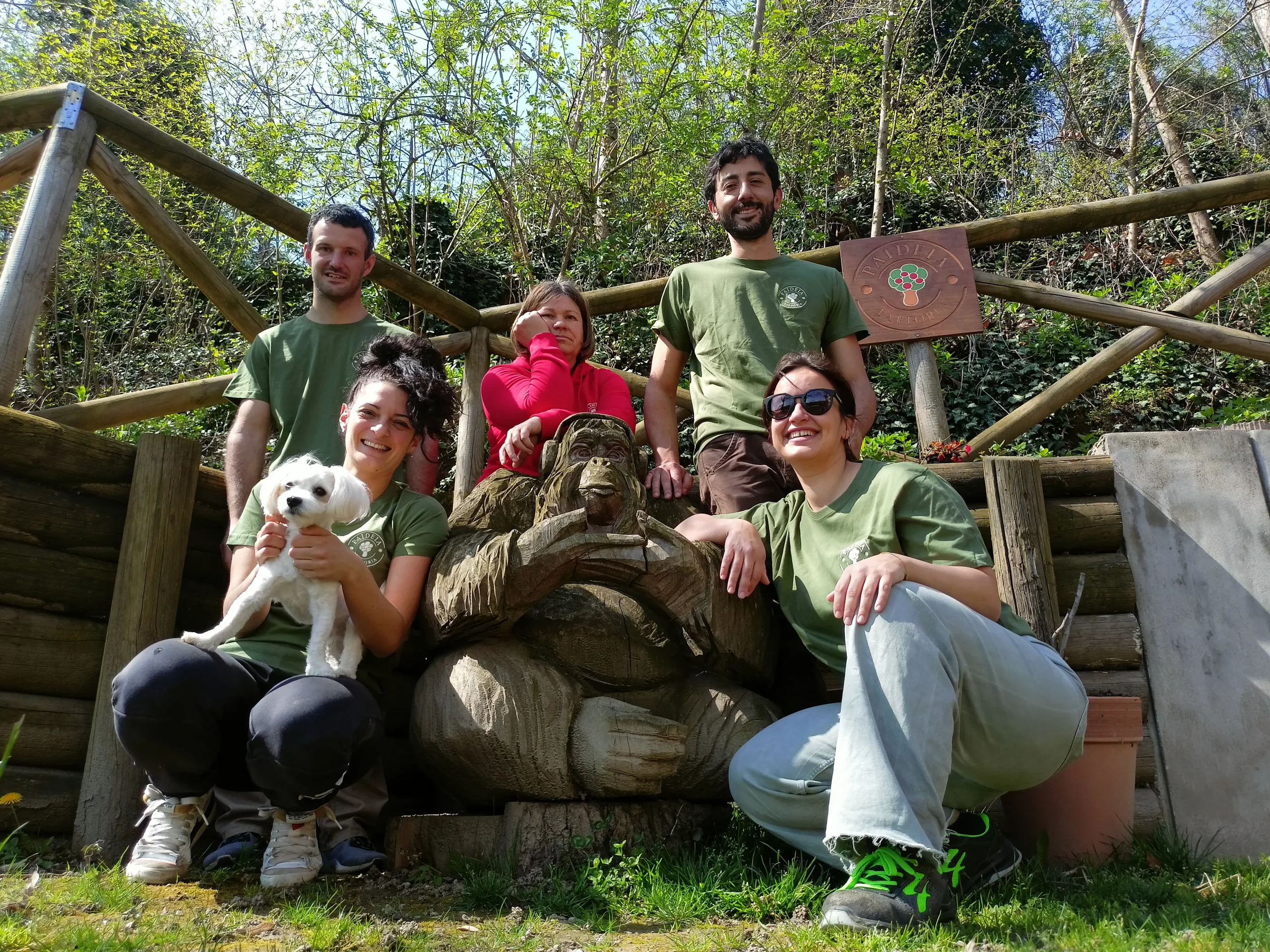 alcune persone guardano in camera e sorridono, dietro ci sono una staccionata e degli alberi
