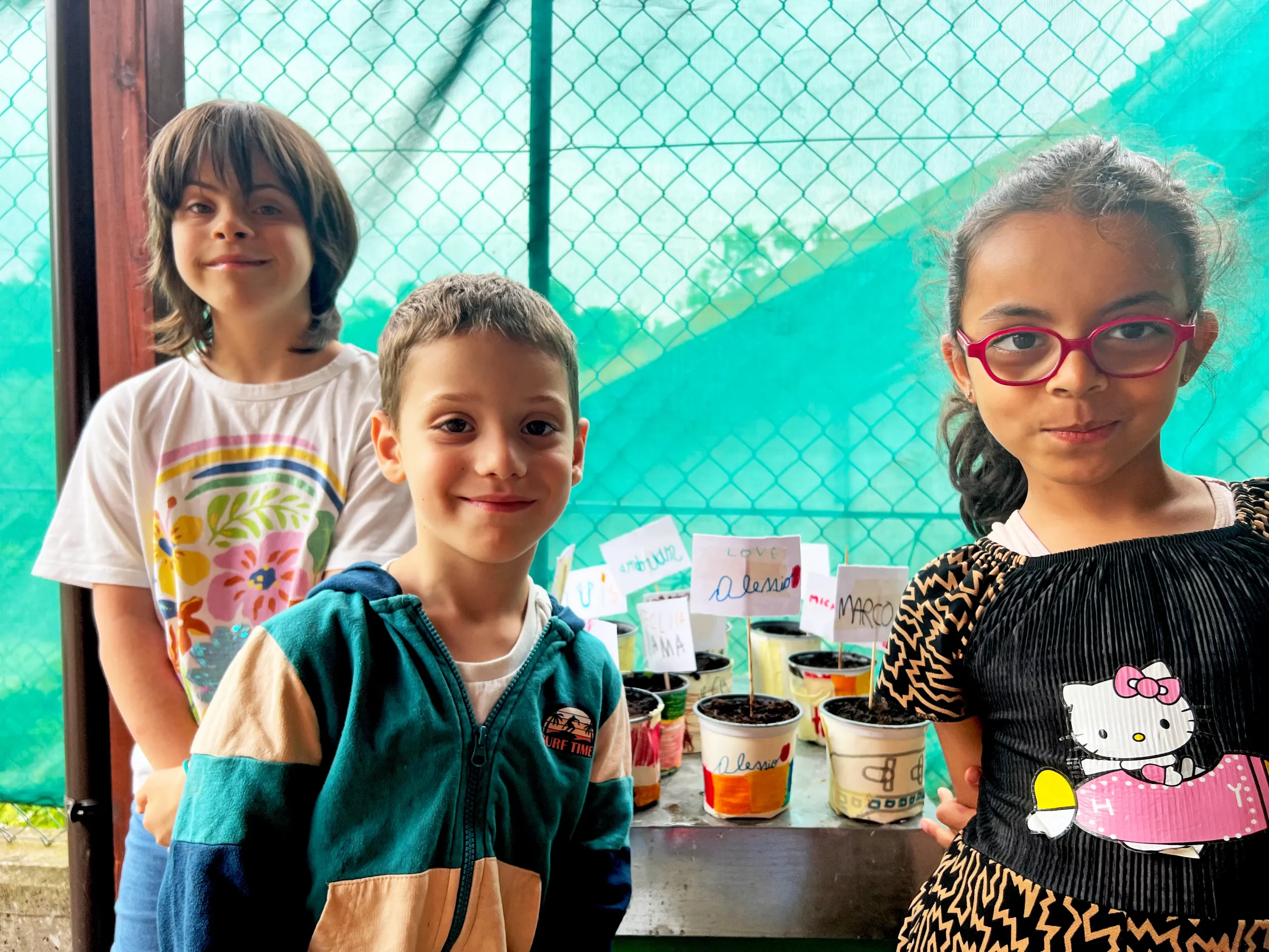 bambini guardano in camera e sorridono, su un ripiano sono appoggiati dei vasetti con i nomi