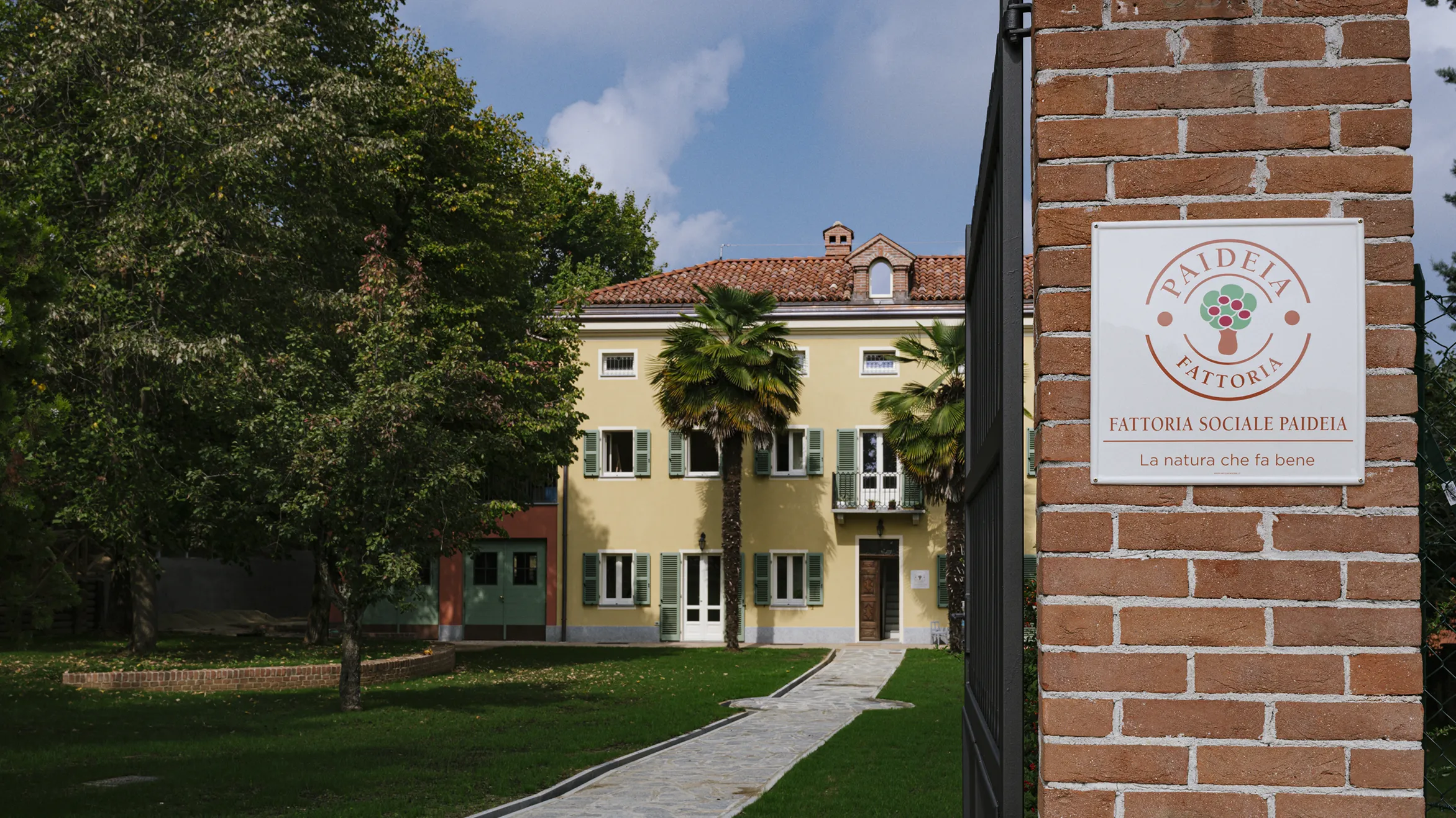 edificio colorato e prato antistante. in primo piano la targa della fattoria sociale