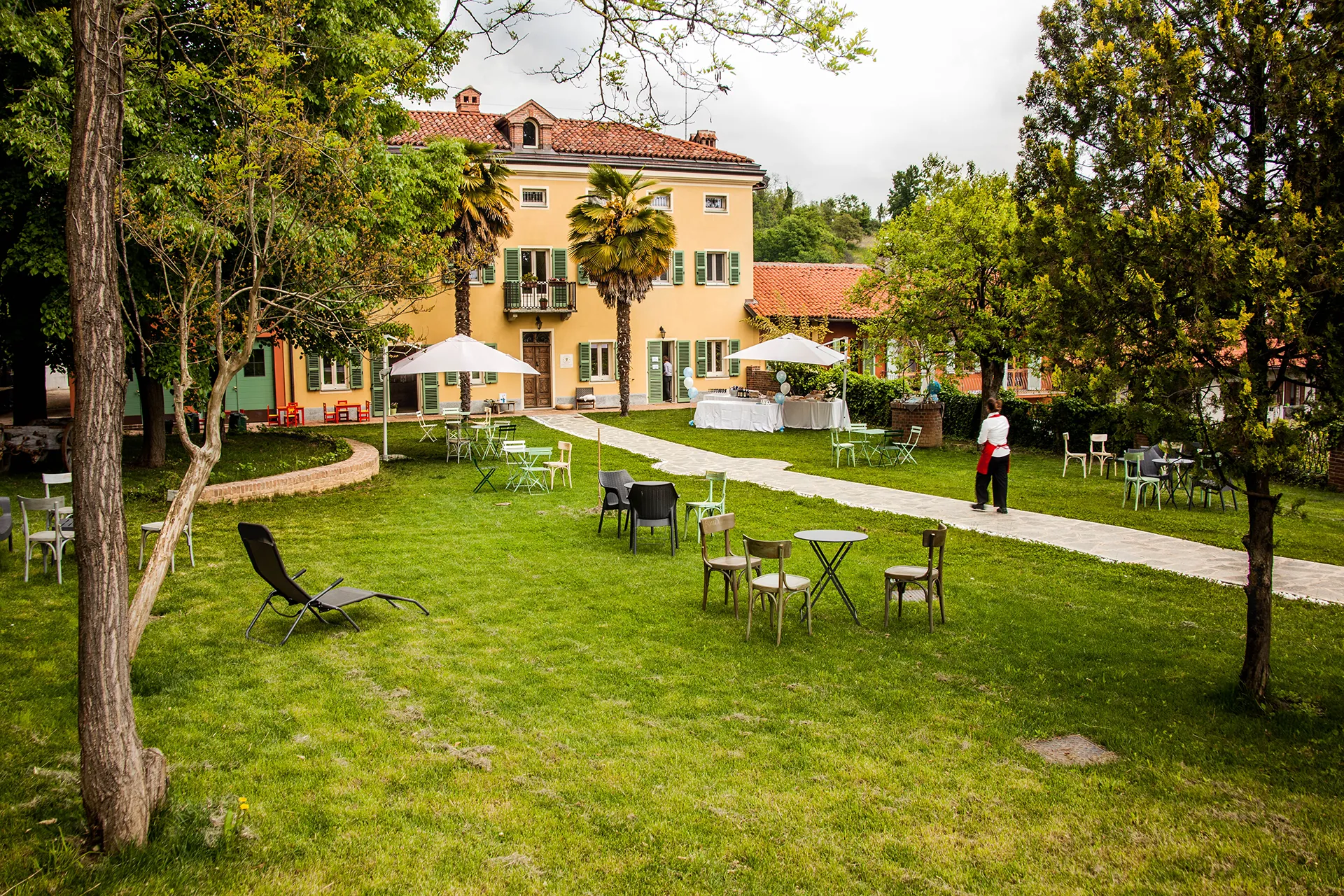 vista di un edificio colorato e dell'ampio prato antistante, con alberi, tavoli e altri arredi da esterno