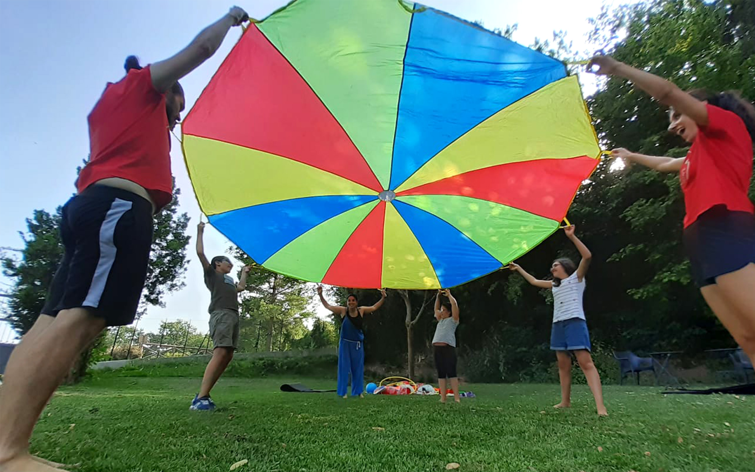 alcuni ragazzi in cerchio tengono sollevato un telo rotondo multicolore